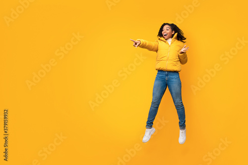 Excited African Woman In Jacket Pointing Finger Over Yellow Background