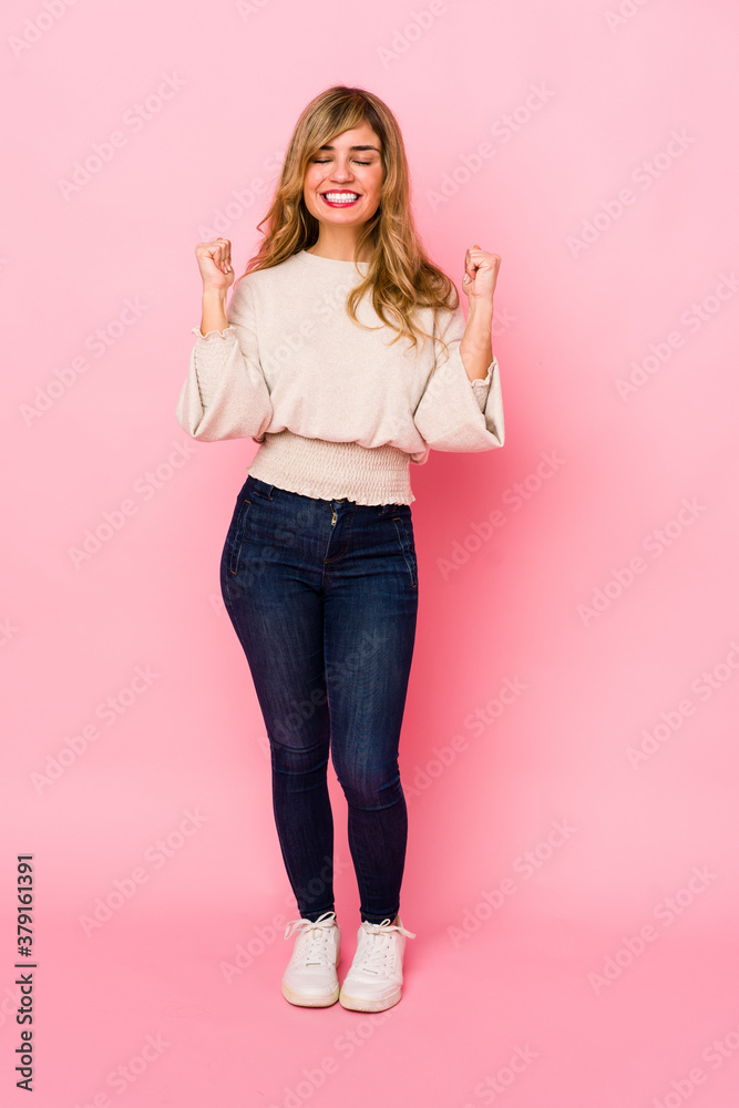 Young blonde caucasian woman standing over a pink background raising fist, feeling happy and successful. Victory concept. Young blonde caucasian woman standing over a pink background raising fist, feeling happy and successful. Victory concept.