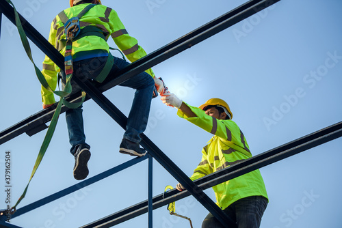 Two Asian construction workers wore safety clothing and safety harnesses to work on the steel roof structure.