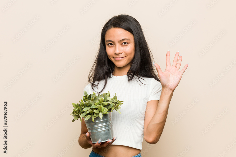 Young asian woman holding a plant smiling cheerful showing number five with fingers. Young asian woman holding a plant smiling cheerful showing number five with fingers.