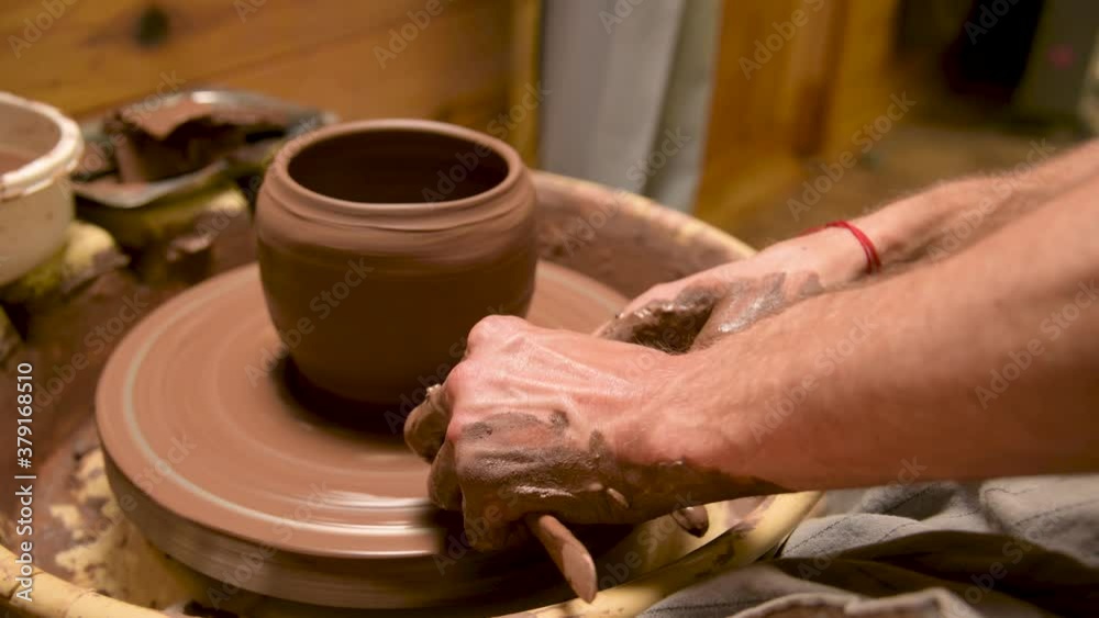 Male hands making a clay bowl on a potter's wheel. Handicraft and production of exclusive tea ware made of clay Male hands making a clay bowl on a potter's wheel. Handicraft and production of exclusive tea ware made of clay