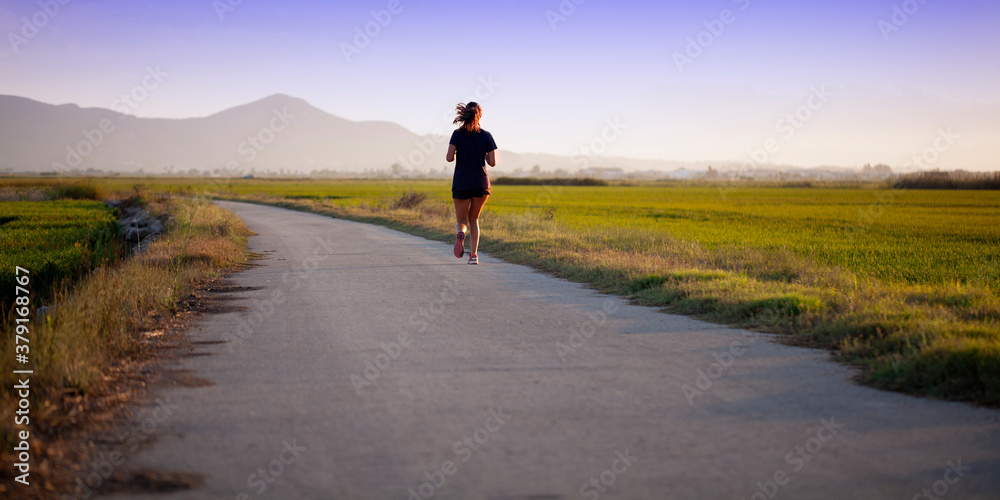 Mujer joven corriendo por camino solitario al atardecer