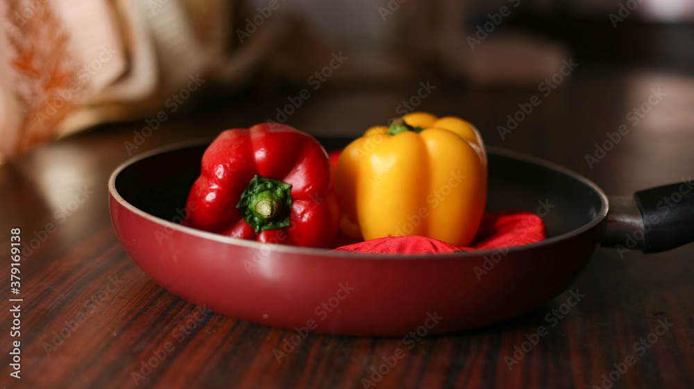 Closeup view of red and yellow color bell peppers in cooking pan with wooden background Closeup view of red and yellow color bell peppers in cooking pan with wooden background