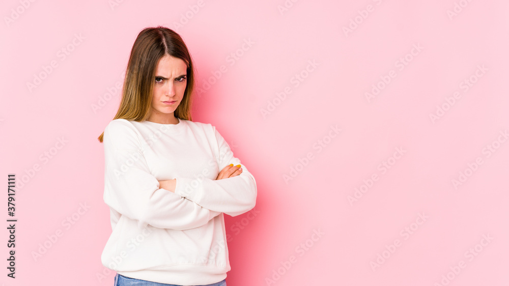 Young caucasian woman isolated on pink background frowning face in displeasure, keeps arms folded. Young caucasian woman isolated on pink background frowning face in displeasure, keeps arms folded.
