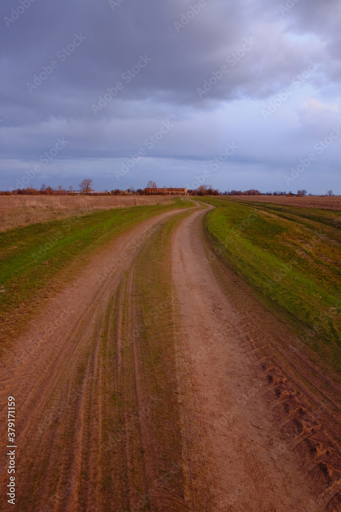 Long dirt road in the fields. Cloudy evening landscape.
