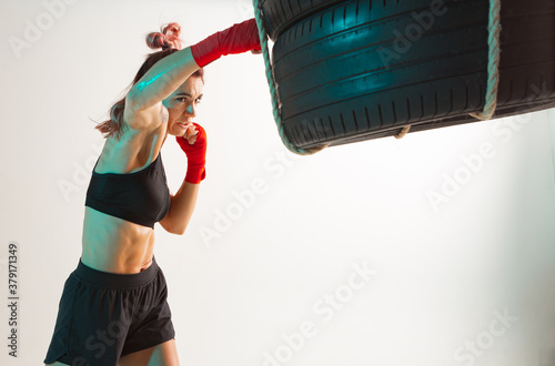 Athletic girl in stylish sportswear boxing on punching bag isolated on white. Women's sport and motivation concept