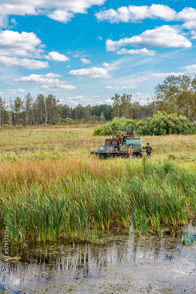 Fototapeta premium Hunters and an old military tracked tractor built in the 70s of the last century in the Soviet Union on a hunting trip in the autumn forest