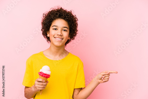 Kid boy holding an ice cream isolated smiling and pointing aside, showing something at blank space.