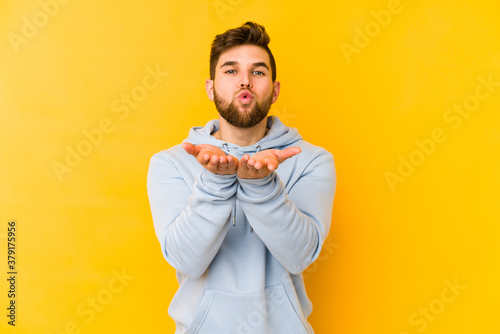 Young caucasian man isolated on yellow background folding lips and holding palms to send air kiss.