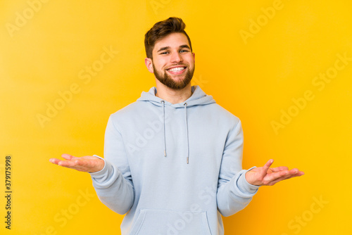 Young caucasian man isolated on yellow background showing a welcome expression.