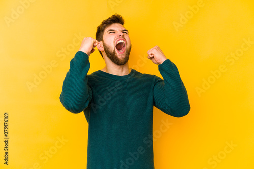 Young caucasian man isolated on yellow background raising fist after a victory, winner concept.
