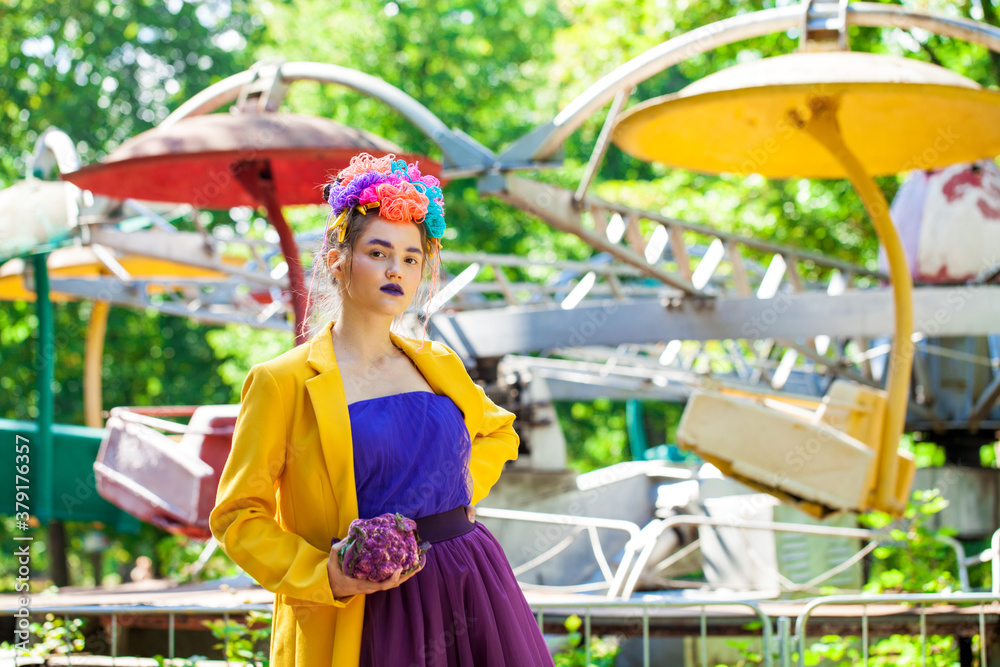 Young beautiful model in stylish clothes posing against the backdrop of attractions in an amusement park