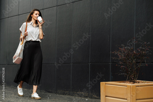 Mature business woman walking on the side of a street, drinking coffee photo