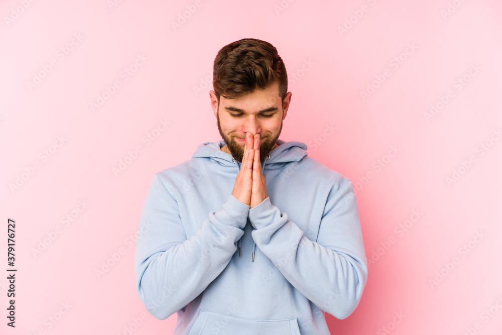 Young caucasian man isolated on pink background holding hands in pray near mouth, feels confident. Young caucasian man isolated on pink background holding hands in pray near mouth, feels confident.