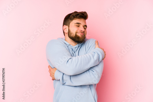 Young caucasian man isolated on pink background hugs, smiling carefree and happy. © Asier