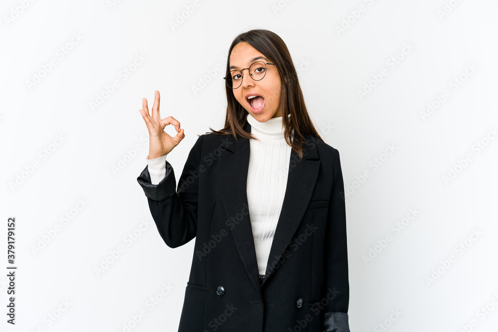 Young mixed race business woman isolated on white background winks an eye and holds an okay gesture with hand. Young mixed race business woman isolated on white background winks an eye and holds an okay gesture with hand.