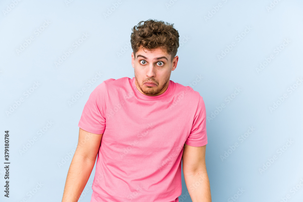 Fototapeta premium Young blond curly hair caucasian man isolated shrugs shoulders and open eyes confused.