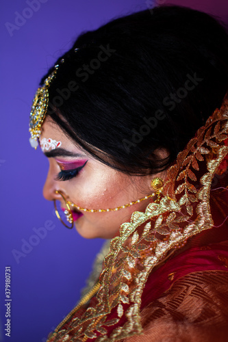 Indian bride dressed in Hindu red traditional wedding clothes sari embroidered with gold jewelry