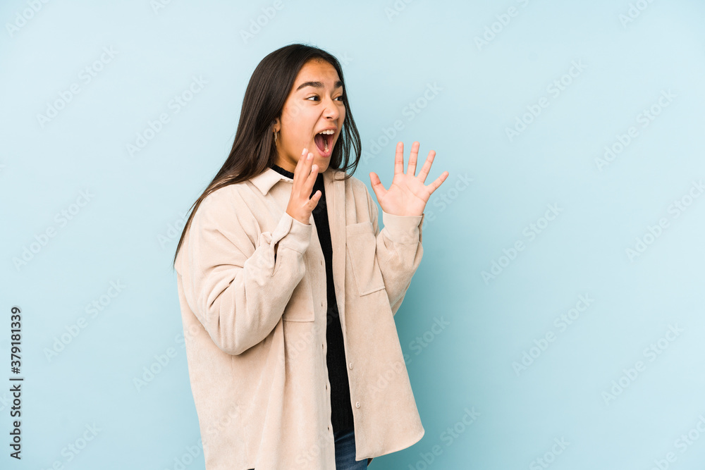 Young woman isolated on a blue background shouts loud, keeps eyes opened and hands tense. Young woman isolated on a blue background shouts loud, keeps eyes opened and hands tense.