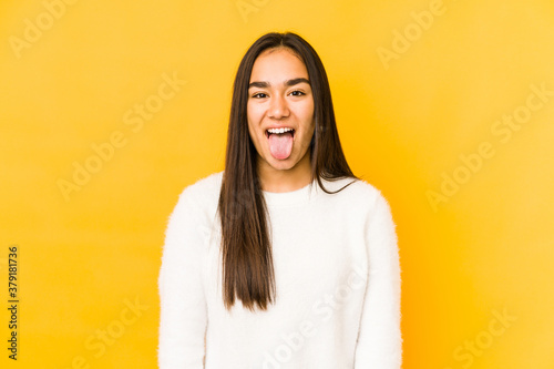 Young woman isolated on a yellow background funny and friendly sticking out tongue. © Asier