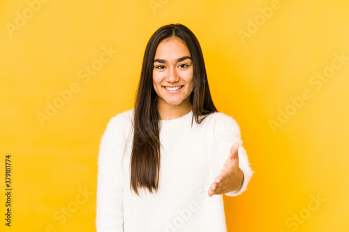 Young woman isolated on a yellow background stretching hand at camera in greeting gesture.