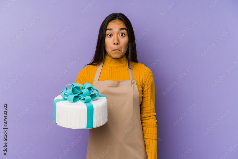 Young asian woman holding a cake isolated shrugs shoulders and open eyes confused. Young asian woman holding a cake isolated shrugs shoulders and open eyes confused.