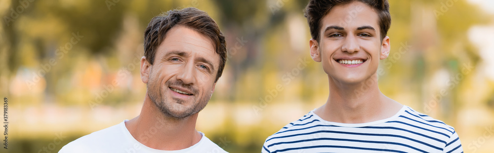 panoramic shot of father and teenager son looking at camera outside panoramic shot of father and teenager son looking at camera outside