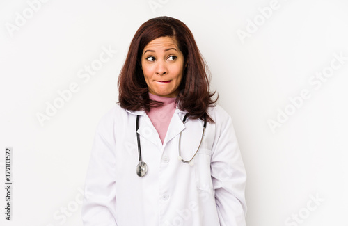 Middle age latin doctor woman isolated confused, feels doubtful and unsure.