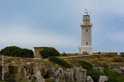 Beautiful cyprus lighthouse at the background of cloudy autumn sky. Grey rocks are in the foreground