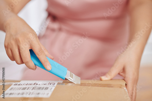 Close-up image of woman using paper knife when opening cardboard box she received at post office