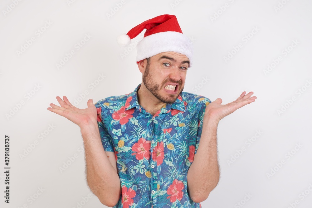 Clueless Young caucasian man wearing hawaiian shirt and Santa hat over isolated white background, shrugs shoulders with hesitation, faces doubtful situation, spreads palms, Hard decision Clueless Young caucasian man wearing hawaiian shirt and Santa hat over isolated white background, shrugs shoulders with hesitation, faces doubtful situation, spreads palms, Hard decision