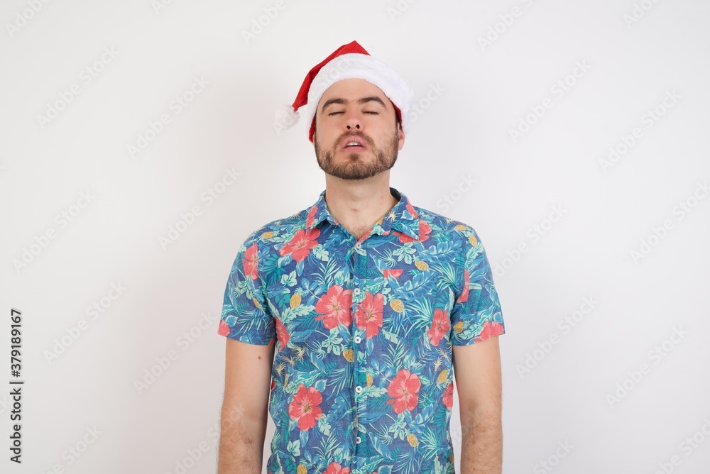 Young caucasian man wearing hawaiian shirt and Santa hat over isolated white background holding finger up having idea and posing Young caucasian man wearing hawaiian shirt and Santa hat over isolated white background holding finger up having idea and posing