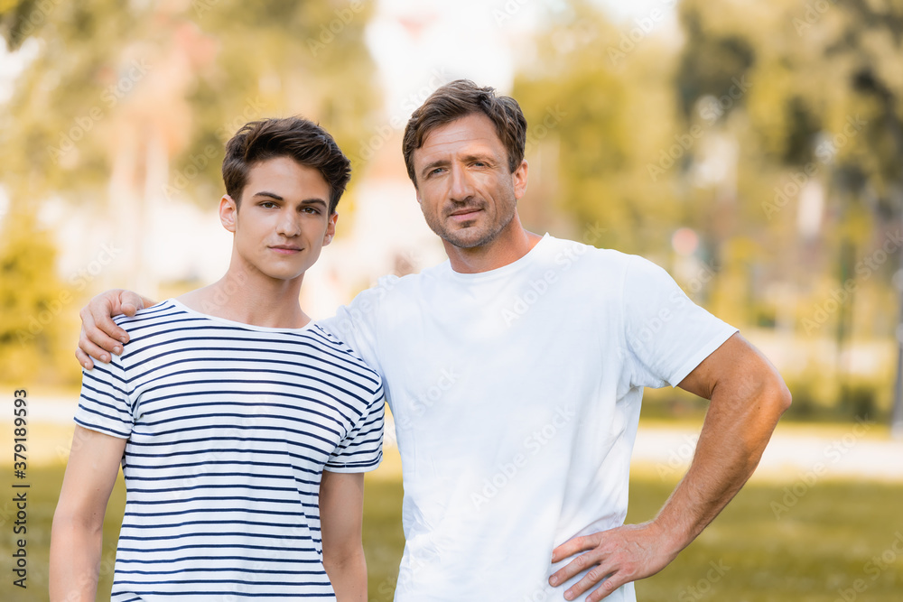 father standing with hand on hip and hugging teenager son outside