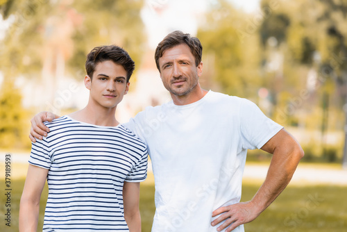 father standing with hand on hip and hugging teenager son outside