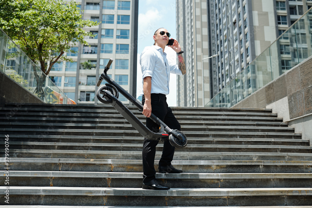 Young stylish man with scooter standing on steps and calling phone Young stylish man with scooter standing on steps and calling phone