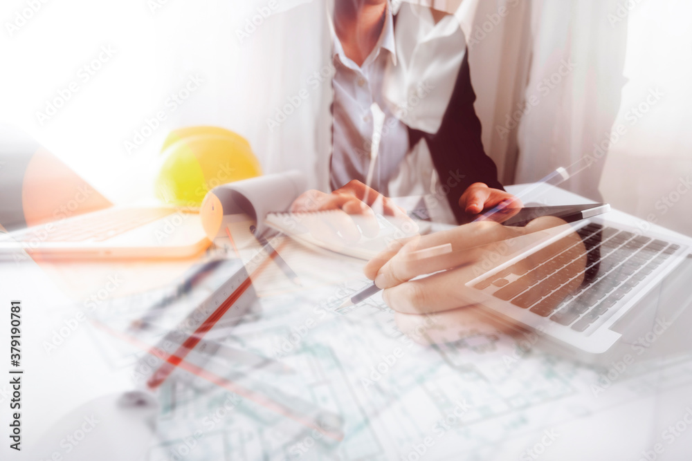 Two colleagues discussing data working and tablet, laptop with on on architectural project at construction site at desk in office Two colleagues discussing data working and tablet, laptop with on on architectural project at construction site at desk in office