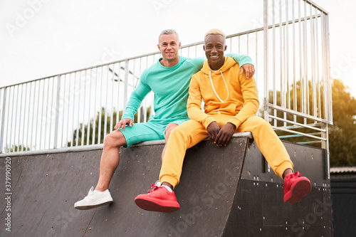 Multi-ethnic friendship Black african-american and caucasian guy friends spending time together on skate park © Andrii