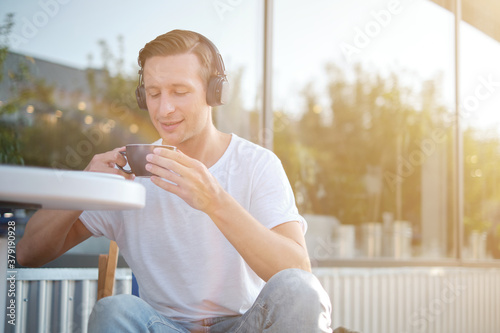 Young attractive man enjoying a cup of aromatic coffee outdoors in sunny weather