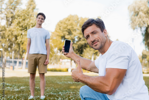 selective focus of father holding smartphone and showing thumb up near teenager son in park © LIGHTFIELD STUDIOS