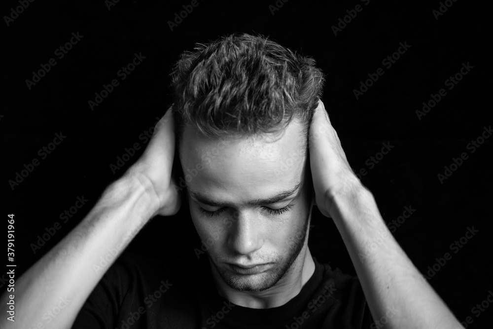 dramatic black and white portrait of sad embarrassed pensive teenager / young guy. Young man, unshaven, with a beard holding his head, black and white photo
