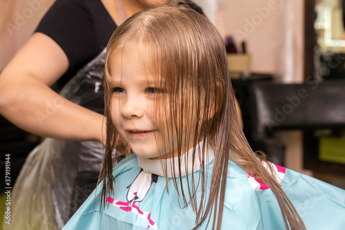 beautiful little red-haired girl at the barber shop.hair cutting process.