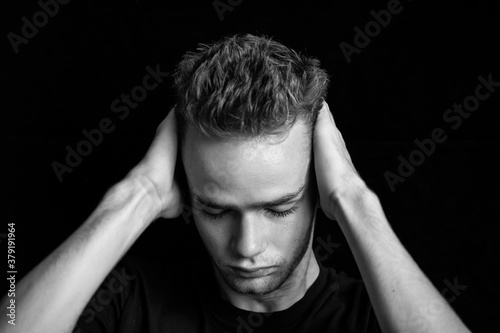 Obraz na płótnie dramatic black and white portrait of sad embarrassed pensive teenager / young guy. Young man, unshaven, with a beard holding his head, black and white photo w salonie