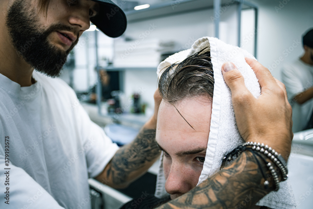Fototapeta premium Tattooed barber with towel drying hair of client before haircut in salon 