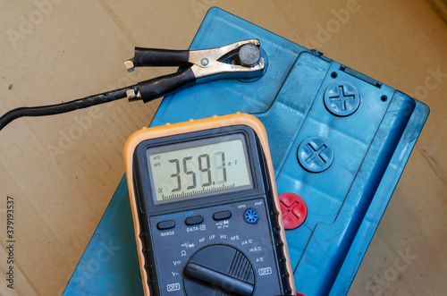 Multimeter lies on top of a car battery. photo