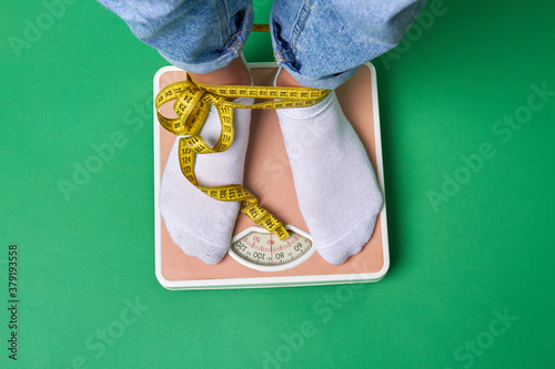 Close-up feet with socks standing on scales. Measuring weight concept. Legs wrapped aroound with yellow tape. Isolated on green background. photo