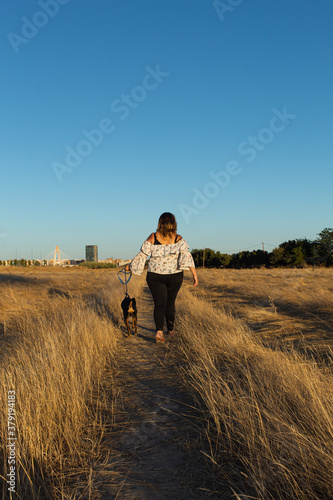 Attractive young woman with a white shirt and wearing a face mouth mask with her dog walking in the countryside. Masks are mandatory outside home during coronavirus COVID-19 outbreak in some countries © Enrique