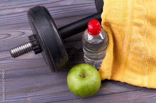 Items for training body on the floor. Green apple, heavy dumbbell and bootle of water with yellow towel. Equipment for workout.