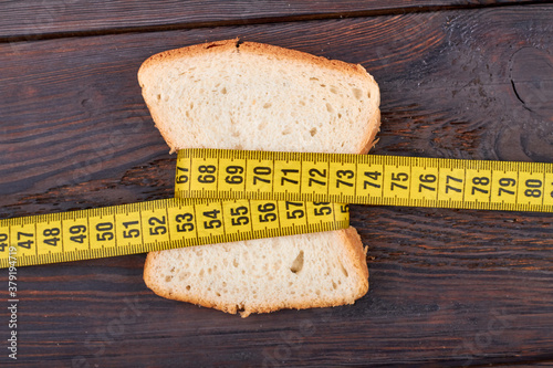 Piece of bread with measure tape. Toast is wrapped aroound with yellow measure tape on the wooden table. Fat losing concept. photo