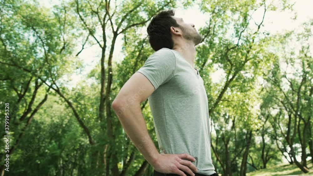 the guy stopped after jogging in the forest park and looks around at the beautiful nature the guy stopped after jogging in the forest park and looks around at the beautiful nature