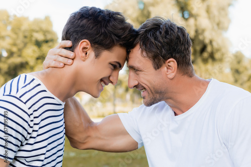 Fotografija side view of joyful father and teenager son looking at each other
